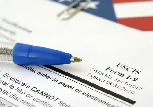 Image of a pen on top of an the I-9 form with a US flag in the background.